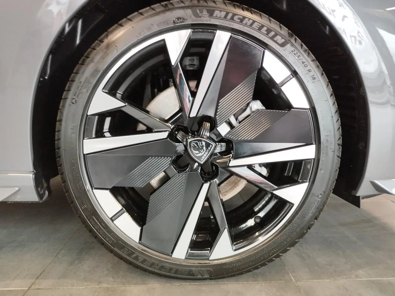 Gros plan sur la jante alliage 18 pouces bi-tons noir et argent avec logo Peugeot, sur roue avant droite gris selenium.