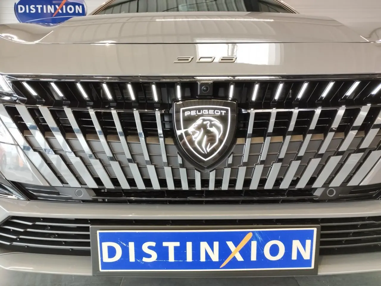 Gros plan sur la calandre avant gris selenium du Peugeot 308 avec logo lion lumineux et plaque Distinxion.