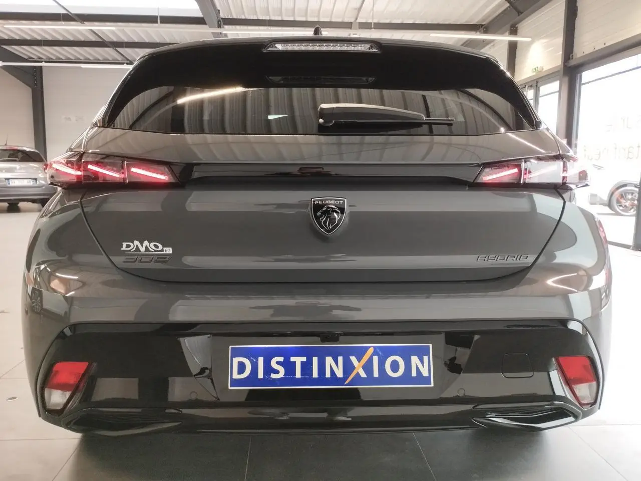 Vue arrière d'une Peugeot 308 hybride gris selenium avec feux arrière LED en forme de griffes et logo Peugeot central.