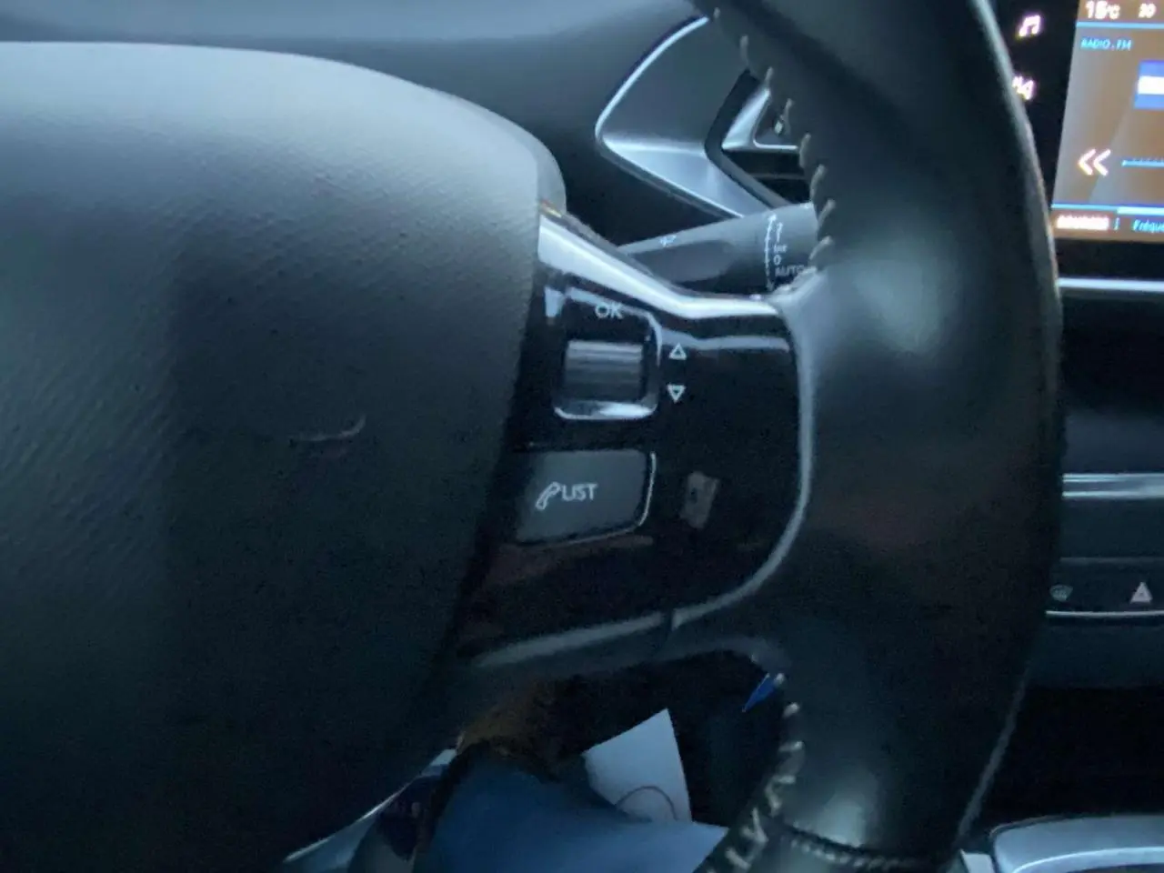 Gros plan sur le volant noir de la Peugeot 308 2020, avec commandes intégrées et écran tactile partiellement visible.