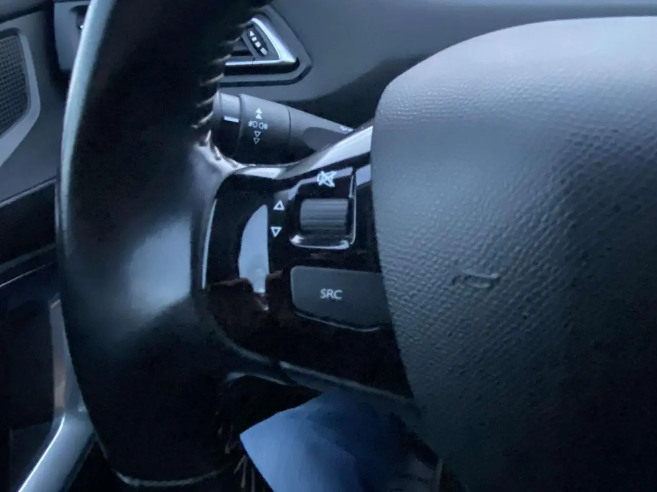 Gros plan sur le volant noir de la Peugeot 308 gris clair, avec commandes audio intégrées sur la branche gauche.