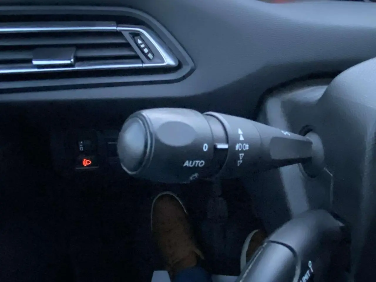 Détail du commodo d'éclairage avec réglage automatique dans l'habitacle d'une Peugeot 308 gris clair.