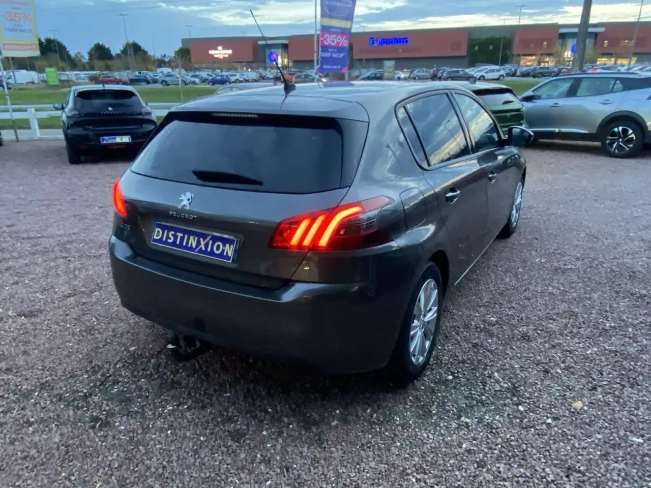 Peugeot 308 gris clair vue 3/4 arrière droit, feux arrière allumés, vitres surteintées, jantes aluminium 16 pouces.