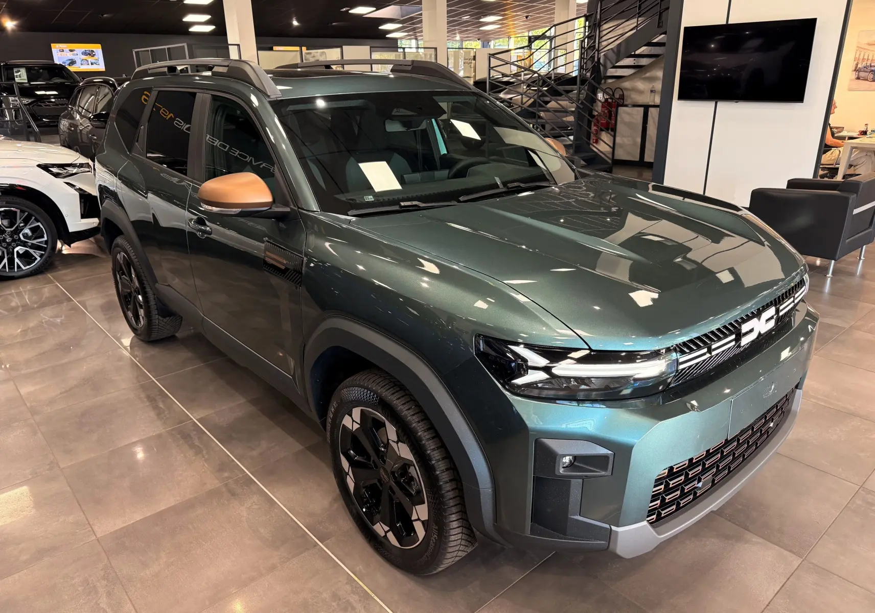 Vue 3/4 avant droit du Dacia Bigster Hybrid-G 150 4x4 en Vert Cèdre avec rétroviseurs bronze et jantes noires bicolores.