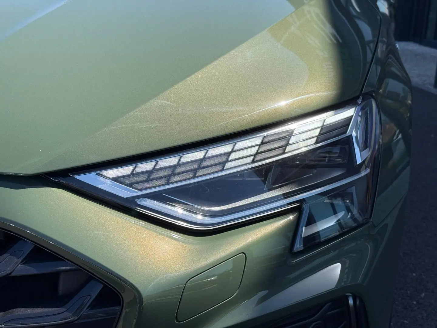 Gros plan sur le phare avant droit de l'Audi A3 Sportback 40 TFSI e vert District métallisé, soulignant ses détails LED.