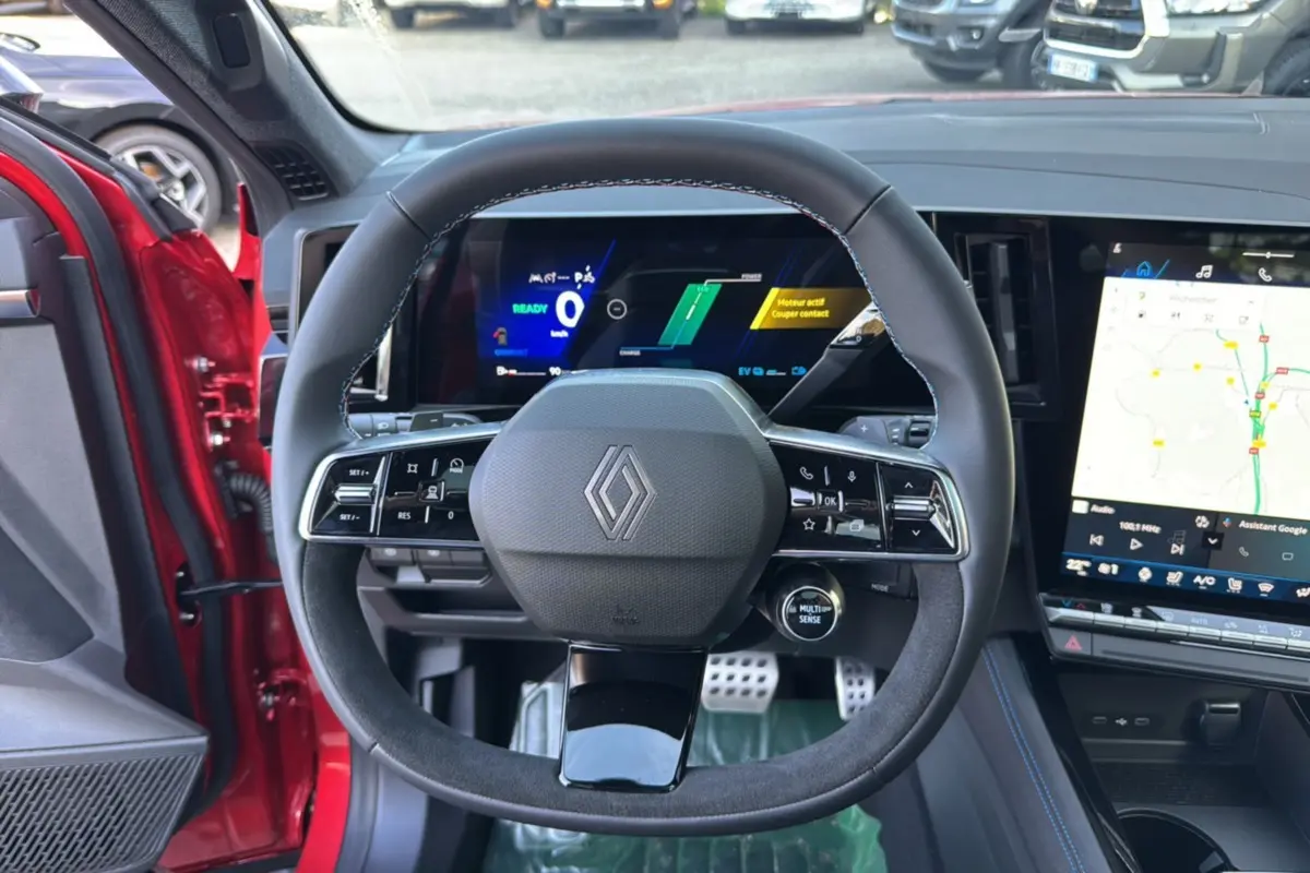 Vue intérieure centrée sur le volant du Renault Austral 2025 rouge toit noir, avec tableau de bord numérique et écran tactile.