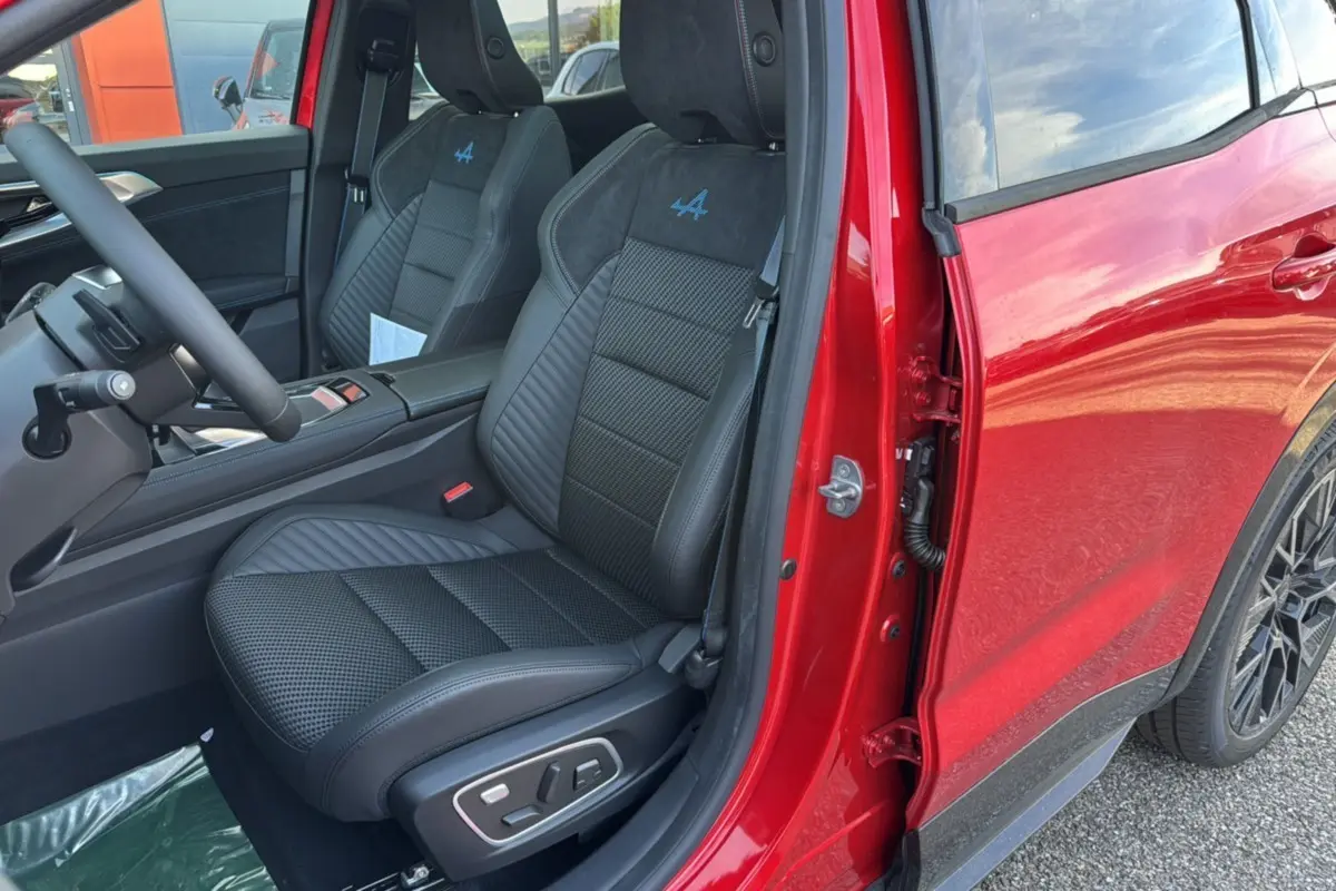 Vue intérieure côté conducteur du Renault Austral 2025 rouge toit noir, sièges sport avec logo Alpine bleu sur appuie-tête.