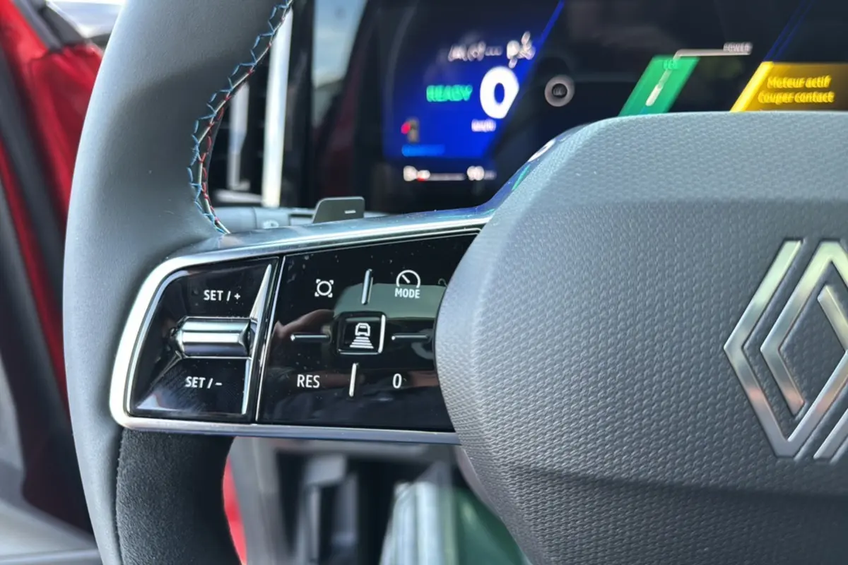 Gros plan sur le volant du Renault Austral 2025 rouge toit noir, avec commandes intégrées et tableau de bord numérique lumineux.