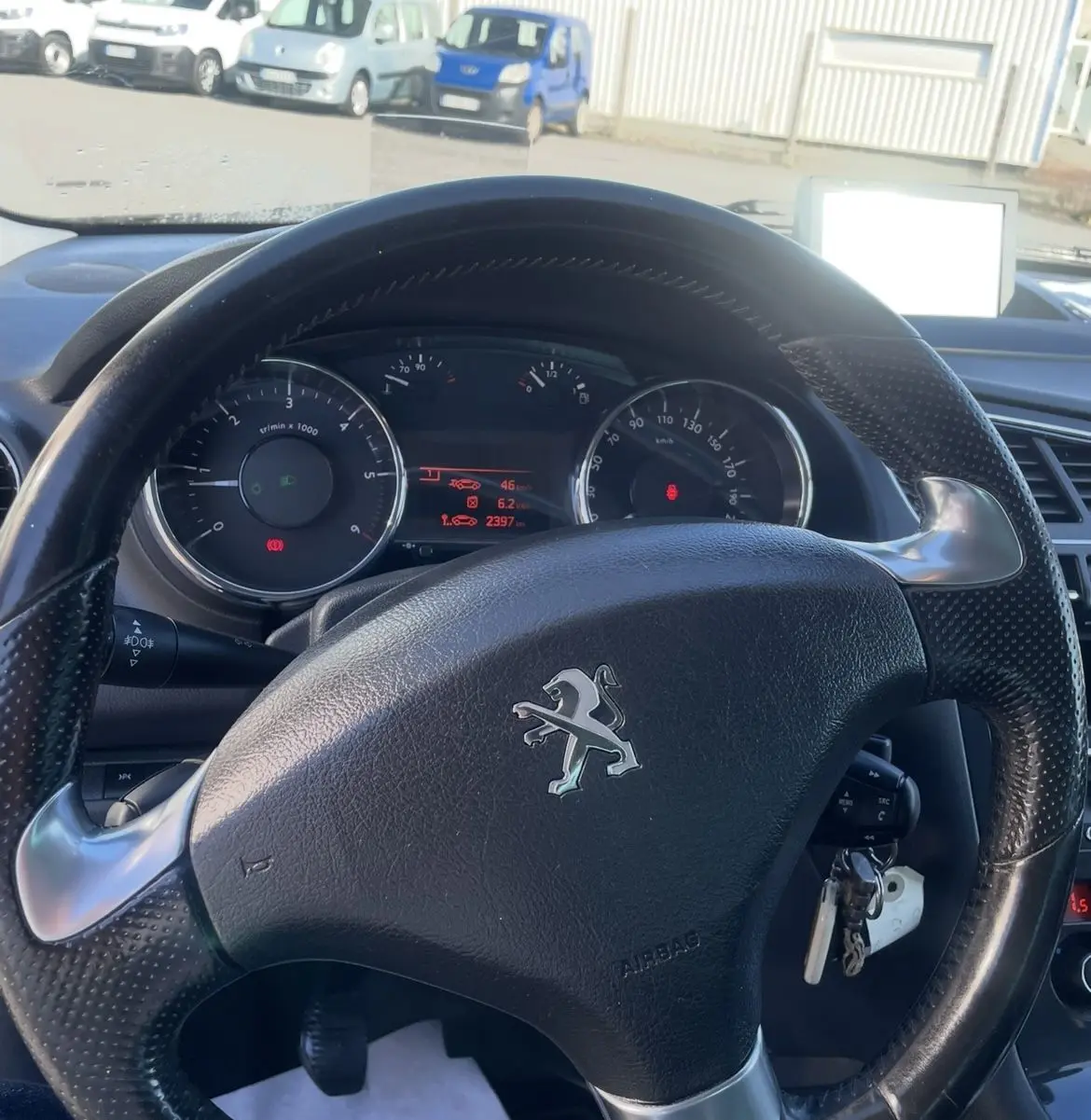 Vue intérieure centrée sur le volant noir d'une Peugeot 3008 2016 avec tableau de bord et clés insérées.