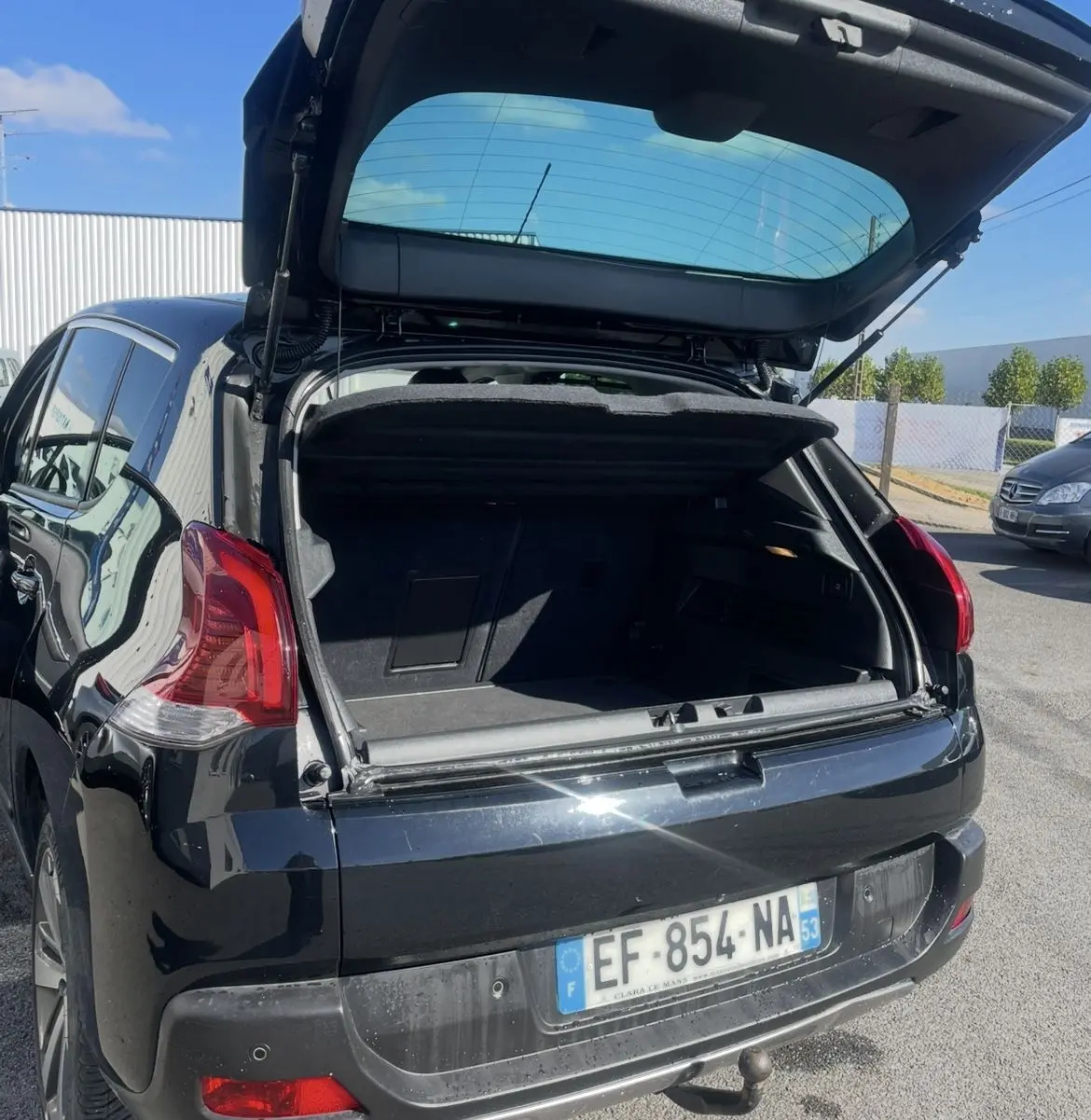 Vue arrière ouverte d'un Peugeot 3008 noir 2016 avec hayon relevé et attelage visible sur parking extérieur.