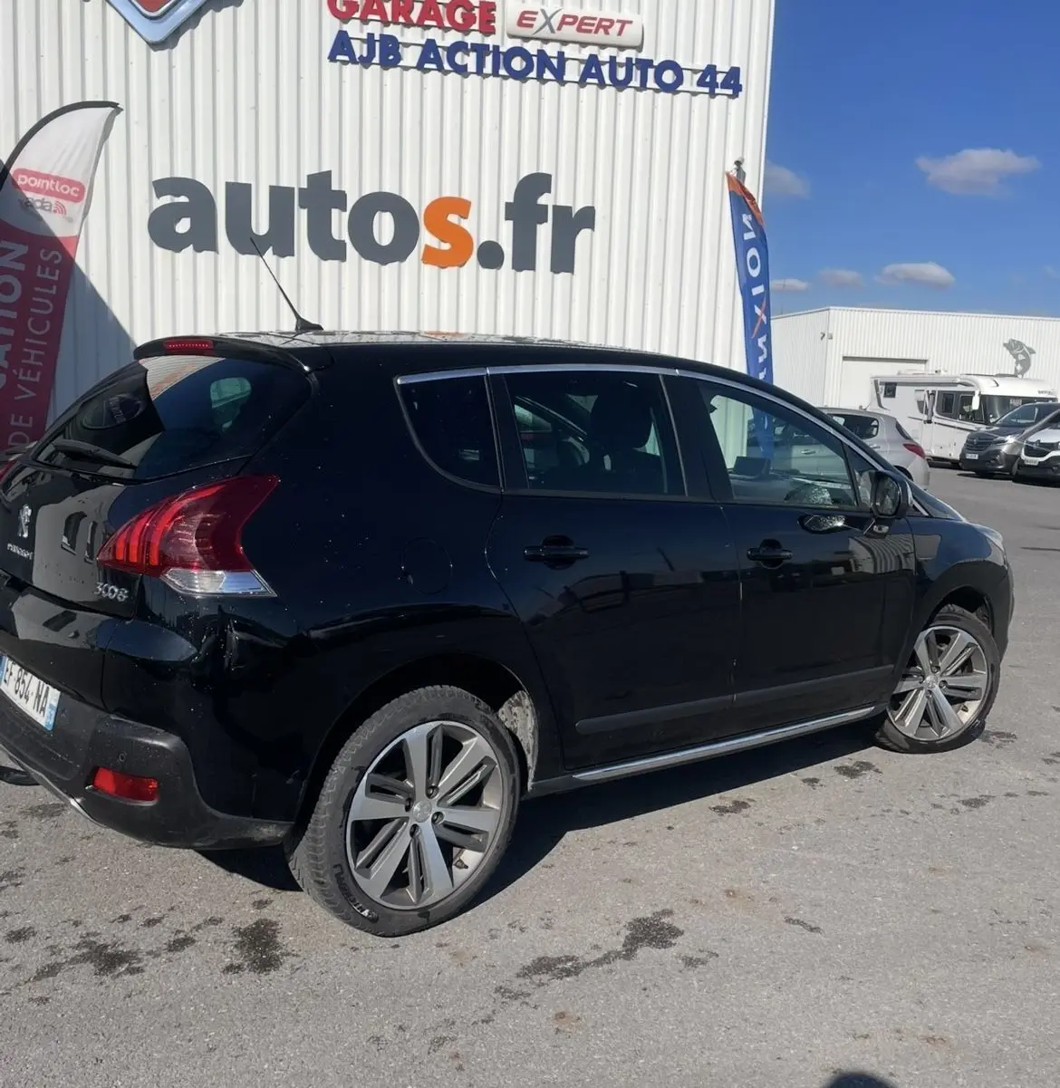 Peugeot 3008 noir vue de trois quarts arrière côté droit, stationnée devant un garage autos.fr par temps ensoleillé.