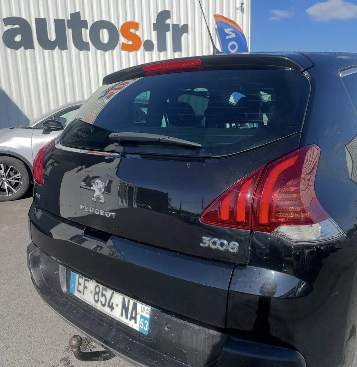 Vue 3/4 arrière droite d'un Peugeot 3008 noir 2016 avec attelage et feux arrière distinctifs au soleil.