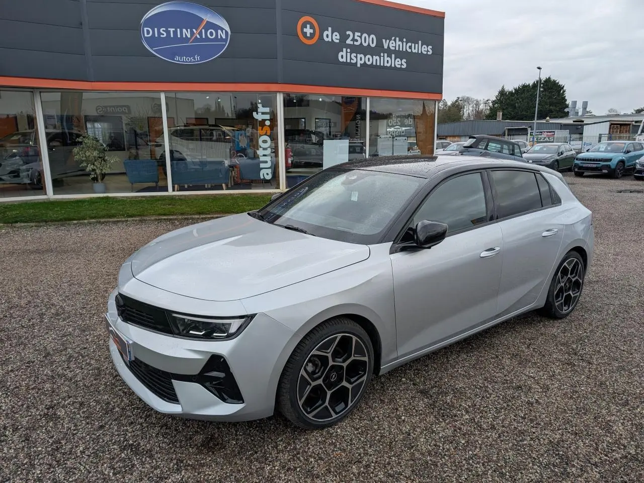 Opel Astra 2024 gris métallisé vue 3/4 avant avec toit noir et jantes alliage pentagonales diamantées.