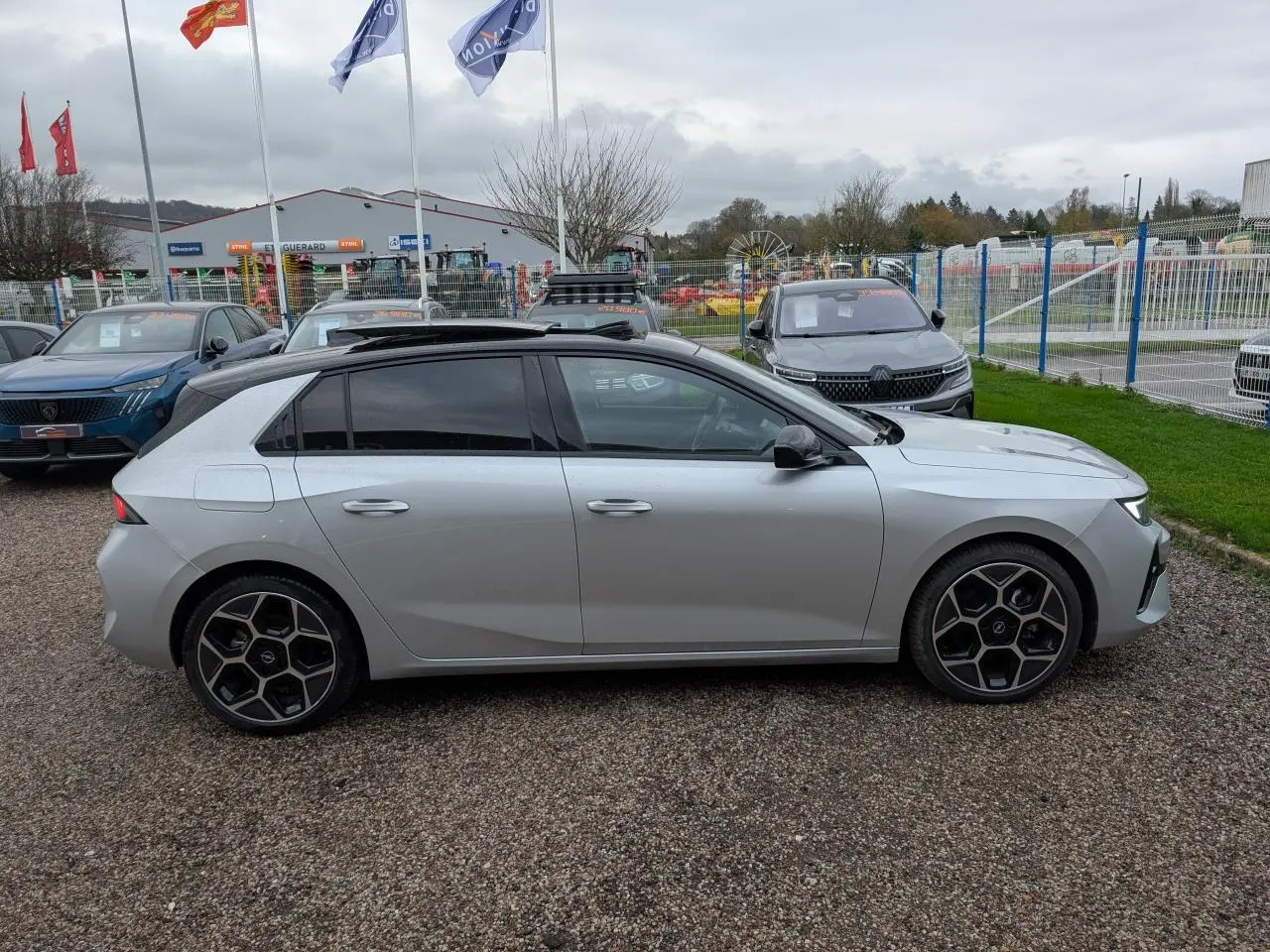 Profil droit d'une Opel Astra gris métallisé avec toit ouvrant panoramique et jantes alliage 18 pouces pentagonales diamantées.