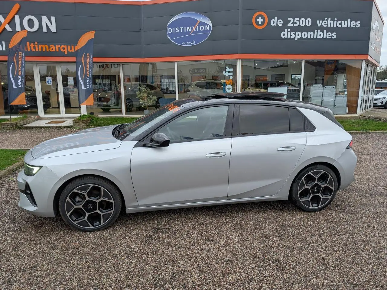 Opel Astra 2024 gris métallisé vue de profil côté gauche avec jantes alliage noires et toit noir panoramique.