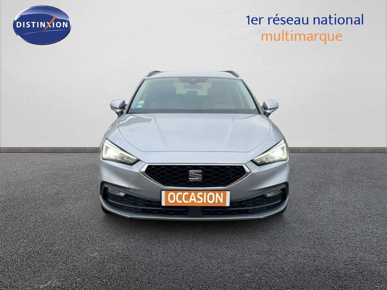 Vue frontale d'une SEAT LEON ST gris urbain métal avec calandre noire et plaque "OCCASION" orange.