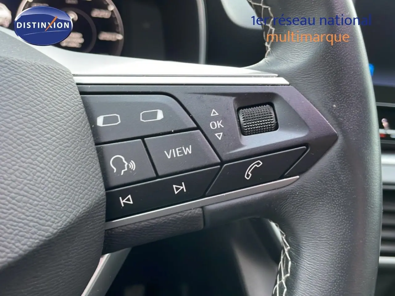 Gros plan sur les commandes au volant en cuir noir du SEAT LEON ST gris urbain, mettant en valeur les boutons multifonctions.