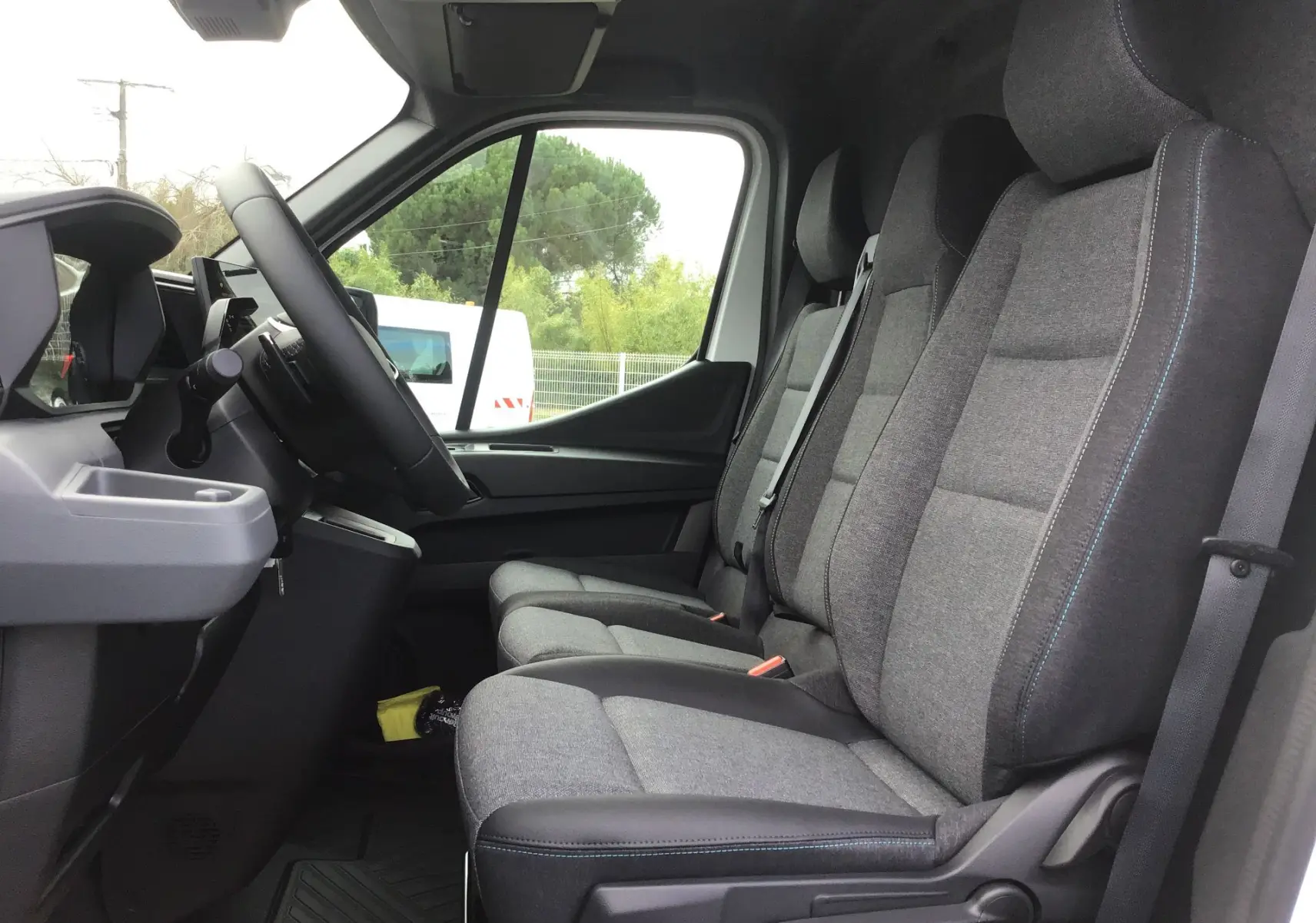 Vue intérieure côté conducteur du Renault Master blanc 2025, montrant la banquette 3 places grise avec coutures bleues et tableau de bord.