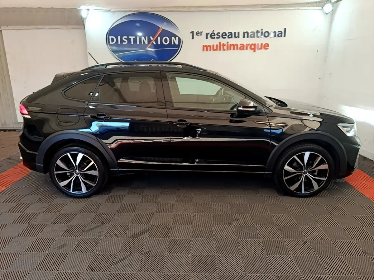 Profil droit d'un Volkswagen Taigo noir 2023 R-Line avec jantes alliage et toit ouvrant en intérieur showroom.