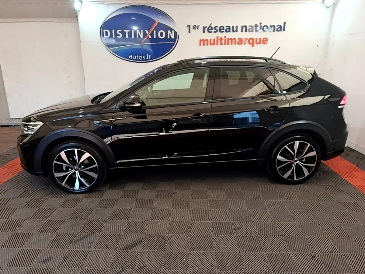 Profil côté gauche du Volkswagen Taigo noir 2023 R-Line avec jantes alliage et rails de toit noirs dans un showroom.