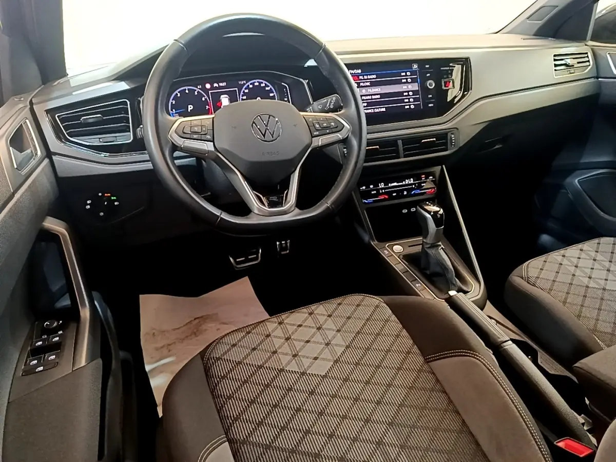 Vue intérieure avant du Volkswagen Taigo 1.5 TSI 150 DSG R-Line avec volant cuir, tableau de bord digital et sièges tissu à motifs.