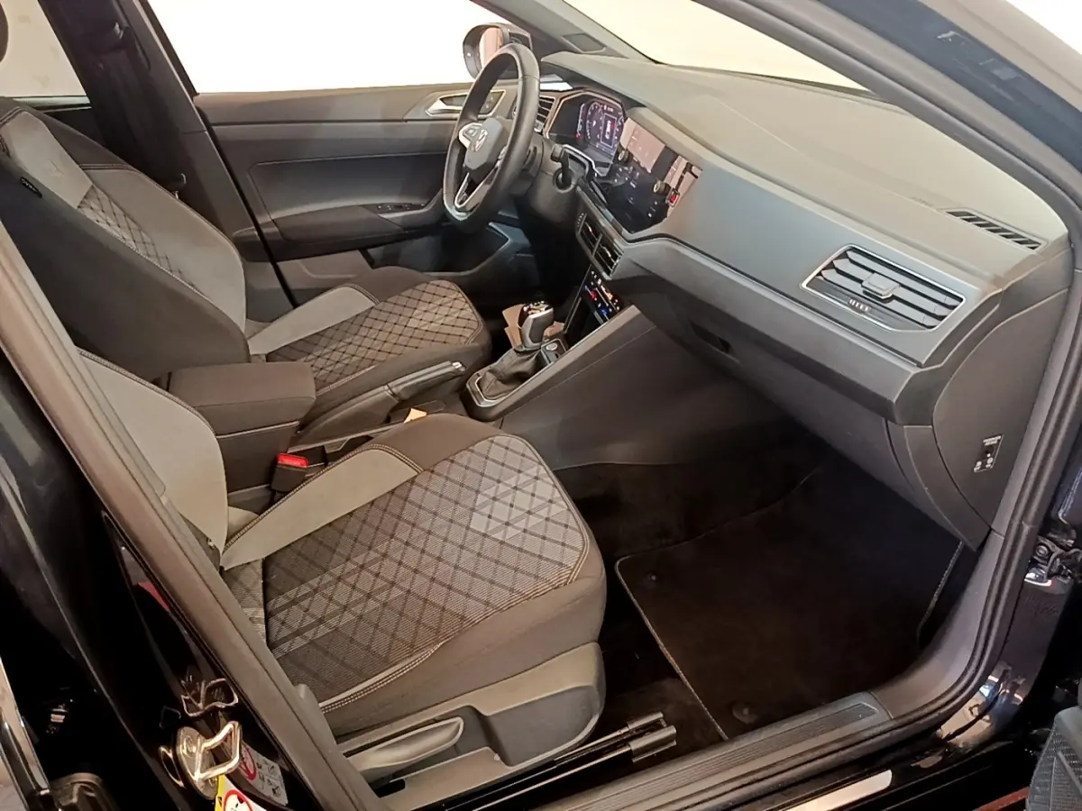 Vue intérieure côté passager avant du Volkswagen Taigo noir 2023, sièges tissu à motifs et tableau de bord moderne.