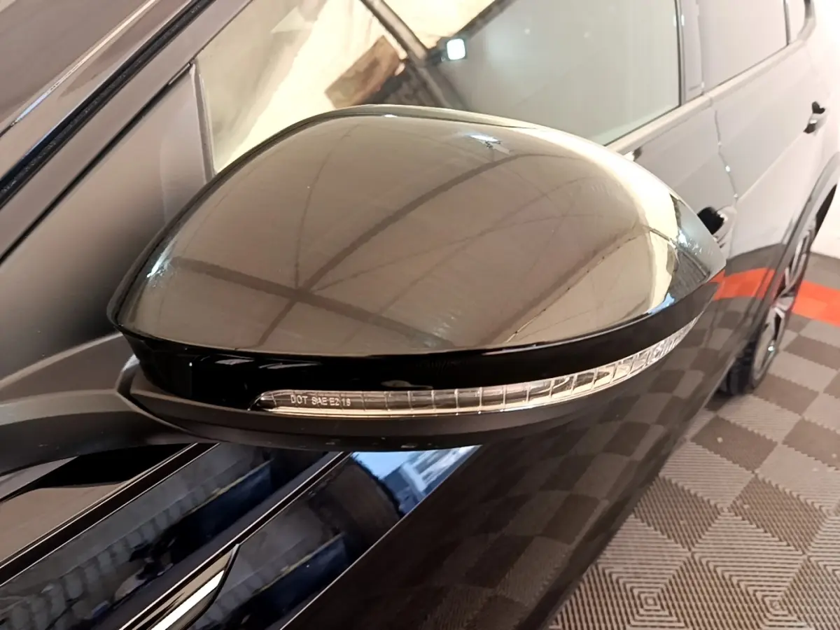 Gros plan sur le rétroviseur droit noir brillant du Volkswagen Taigo 1.5 TSI 150 DSG R-Line avec clignotant intégré.