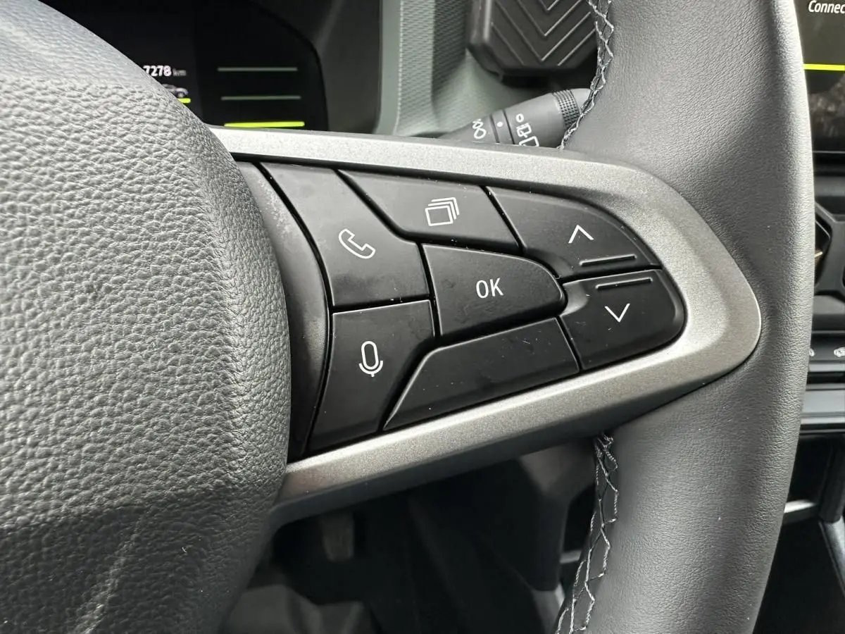 Gros plan sur les commandes au volant à droite du DACIA Duster blanc glacier, montrant les boutons multifonctions et la finition cuir.