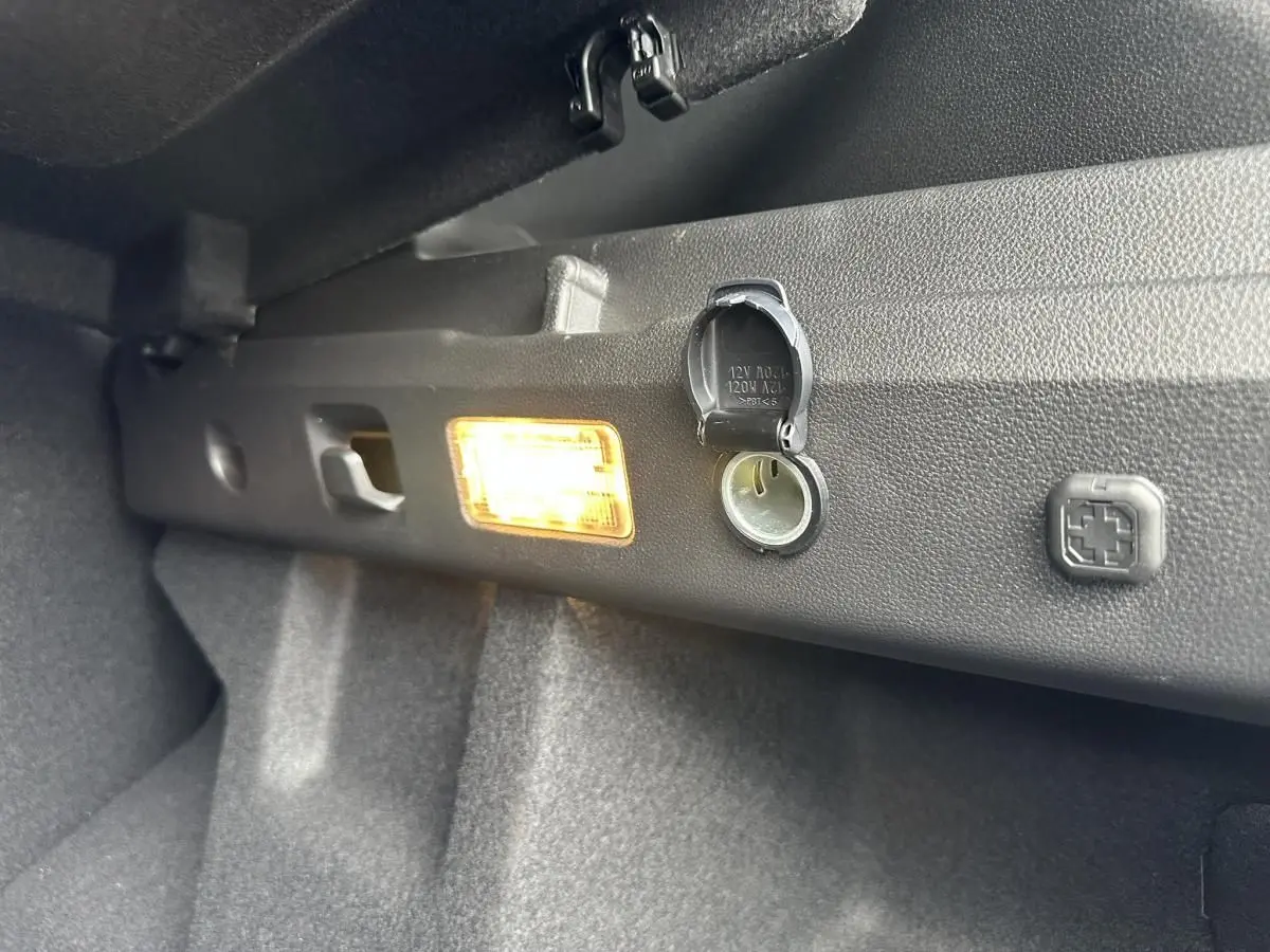 Détail de la prise 12V et de l'éclairage intérieur dans le coffre du Dacia Duster blanc glacier 2025.