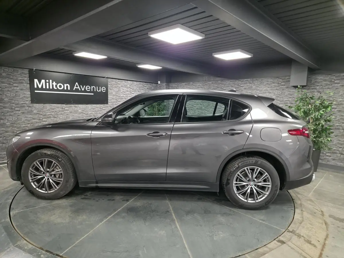 Vue de profil côté gauche d'un Alfa Romeo Stelvio gris métallisé avec jantes alliage 18 pouces dans un showroom.