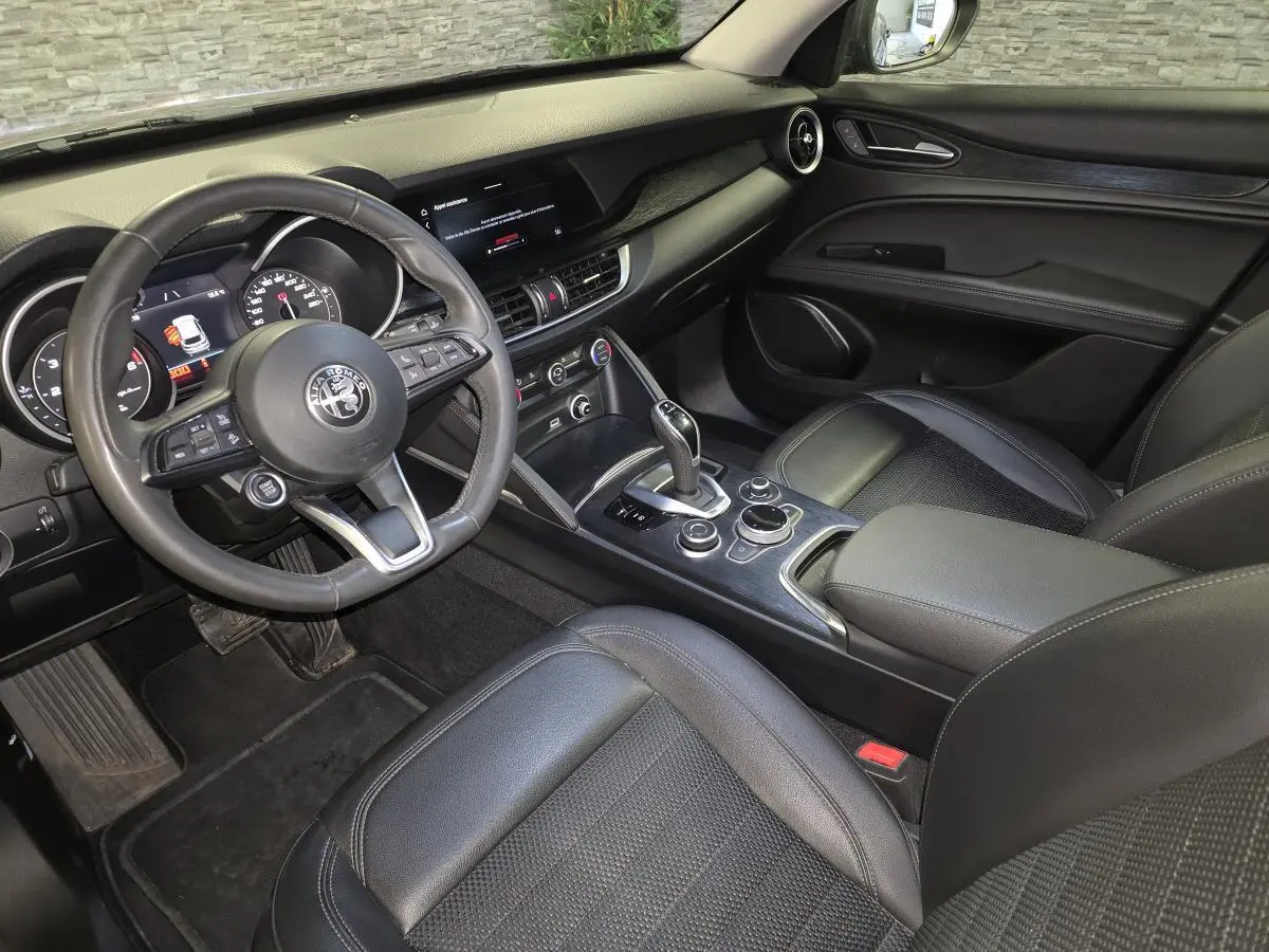 Vue intérieure côté conducteur de l'Alfa Romeo Stelvio 2022, avec volant cuir sport et tableau de bord noir.
