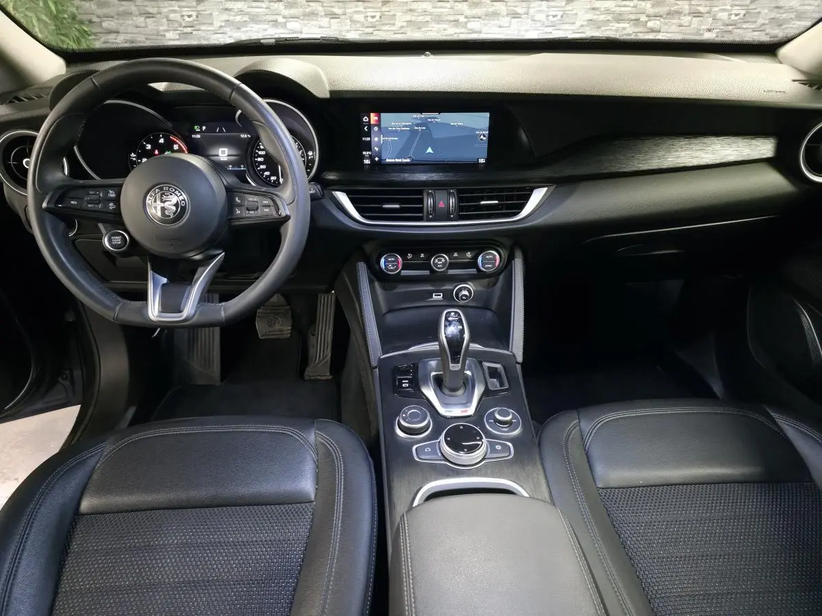Vue intérieure frontale de l'Alfa Romeo Stelvio 2022, tableau de bord noir avec écran tactile et volant cuir sport.