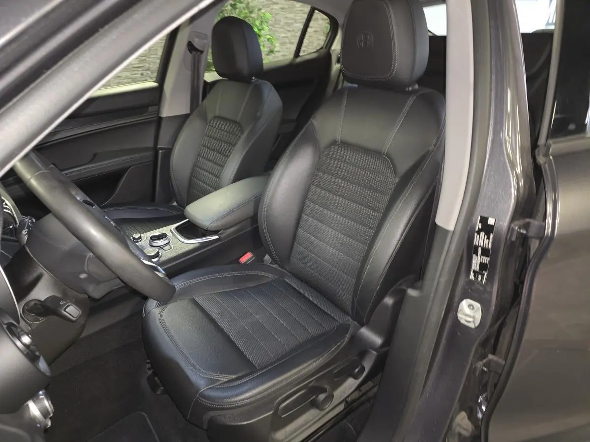Vue intérieure côté conducteur de l'Alfa Romeo Stelvio gris 2022, sièges tissu noir et volant sport cuir.