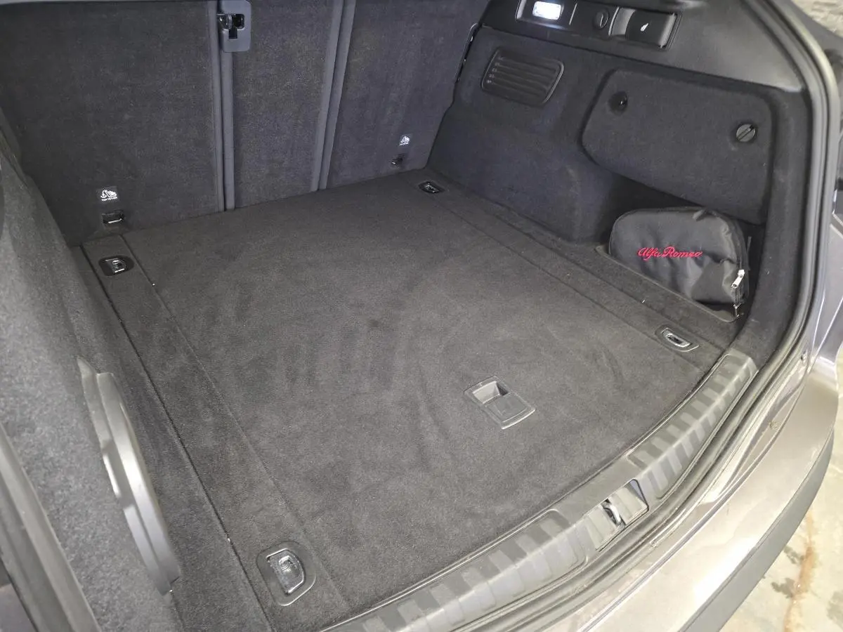 Coffre spacieux de l'Alfa Romeo Stelvio gris, vue arrière avec tapis noir et trousse de secours brodée Alfa Romeo.