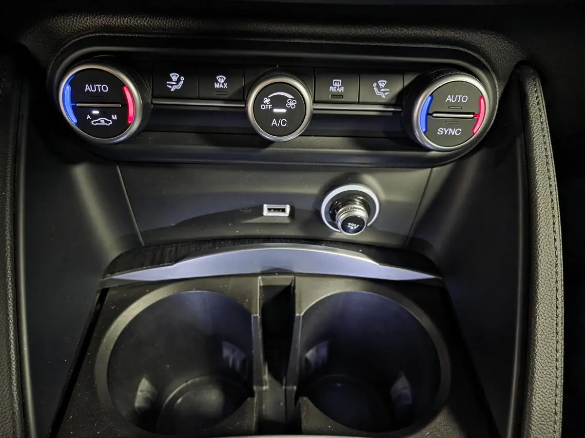 Vue rapprochée de la console centrale de l'Alfa Romeo Stelvio 2022, avec commandes climatisation bi-zone et prises USB/12V.