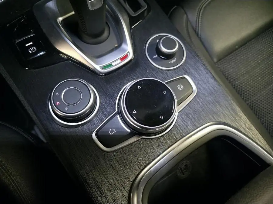 Gros plan sur la console centrale en finition bois foncé de l'Alfa Romeo Stelvio avec commandes rotatives et levier de vitesse.