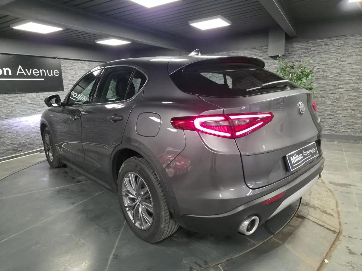 Vue 3/4 arrière droite d'un Alfa Romeo Stelvio gris métallisé avec feux arrière LED et double sortie d'échappement.
