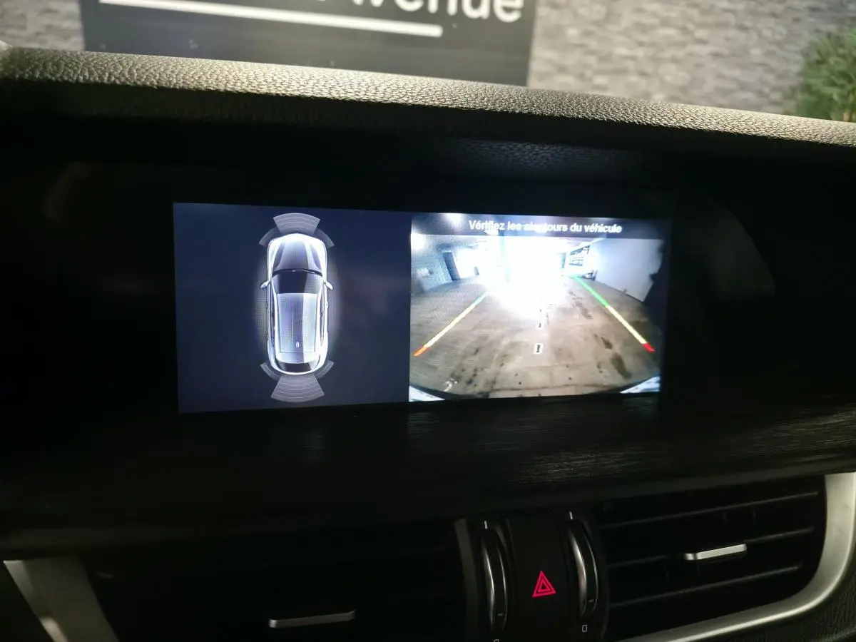 Écran central de l'Alfa Romeo Stelvio gris montrant la caméra de recul et l'alerte de proximité en intérieur.
