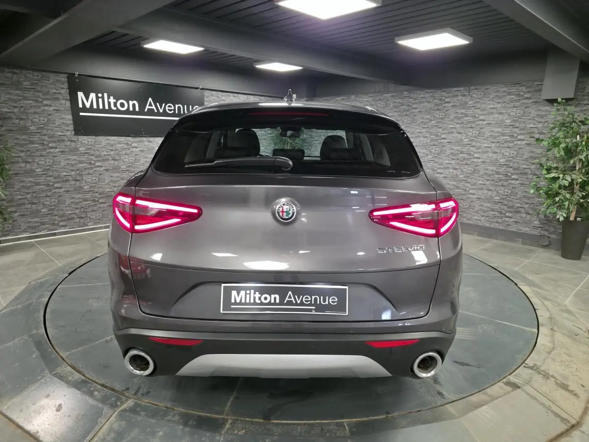 Vue arrière d'un Alfa Romeo Stelvio gris métallisé avec feux LED allumés et double sortie d'échappement.