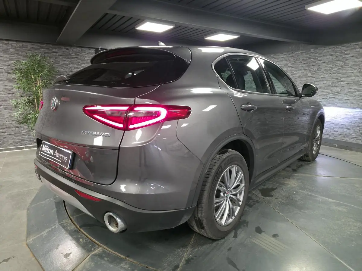 Vue 3/4 arrière droite d'un Alfa Romeo Stelvio gris métallisé avec feux arrière LED et jantes alliage 18 pouces.