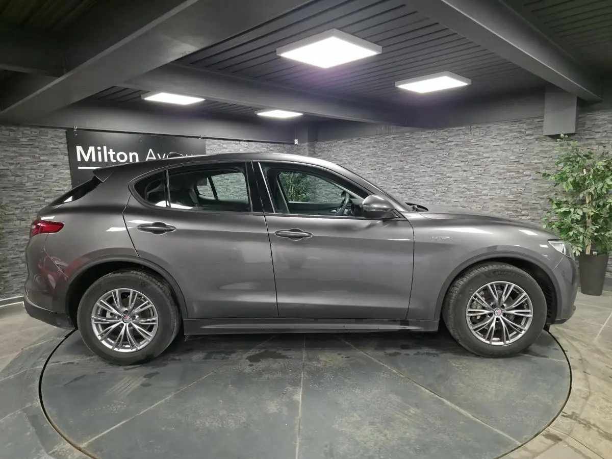 Profil droit d'un Alfa Romeo Stelvio gris métallisé 2022 avec jantes alliage 18 pouces Luxury en intérieur showroom.