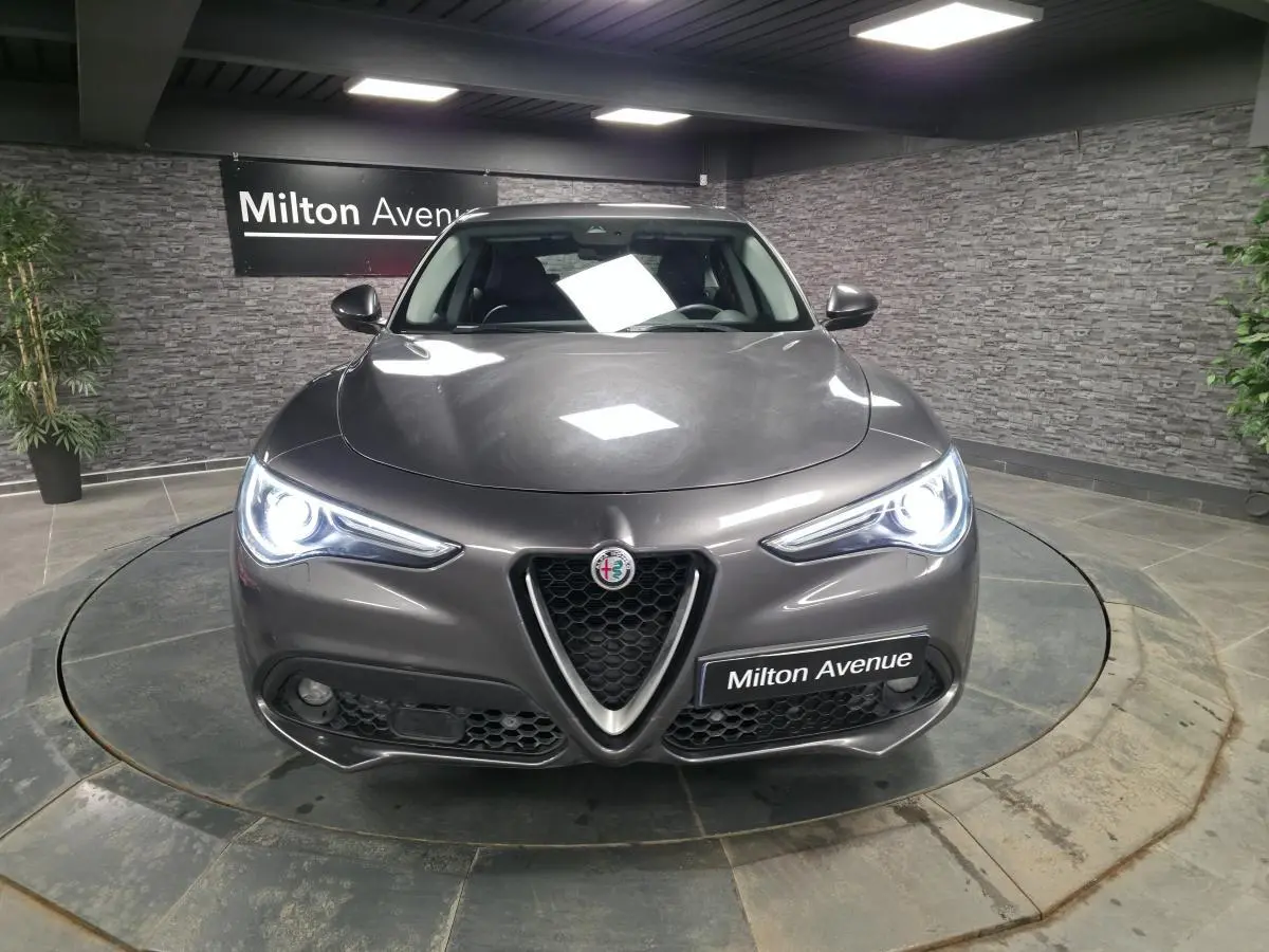 Vue frontale d'une Alfa Romeo Stelvio gris métallisé avec phares LED allumés dans un showroom.