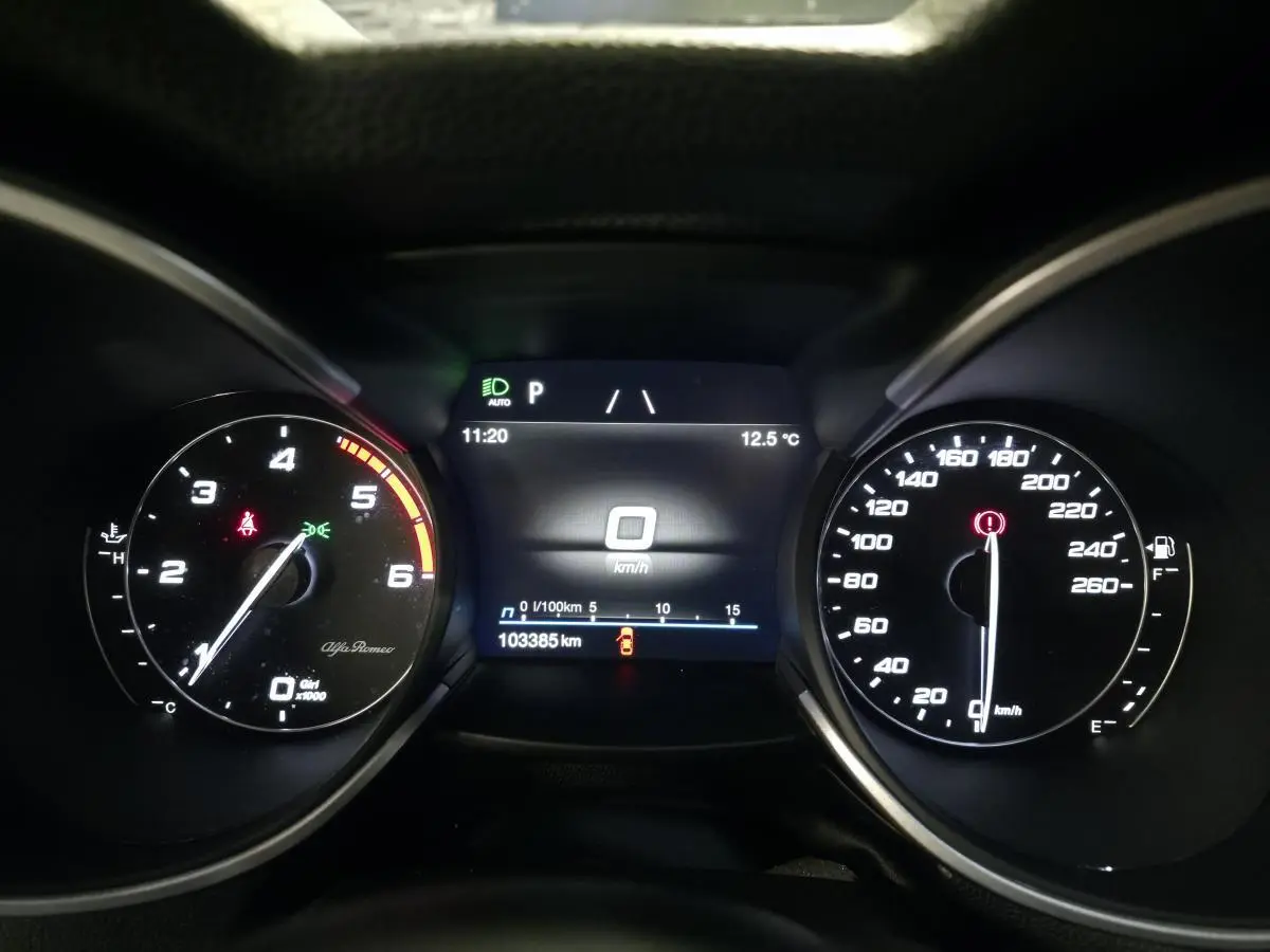 Vue rapprochée du tableau de bord numérique de l'Alfa Romeo Stelvio gris, affichant la vitesse à 0 km/h et 103385 km au compteur.