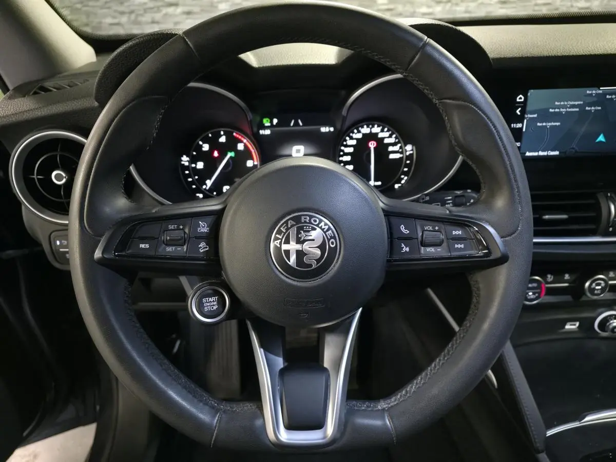Vue rapprochée du volant cuir noir d'Alfa Romeo Stelvio 2022 avec commandes intégrées et tableau de bord numérique.