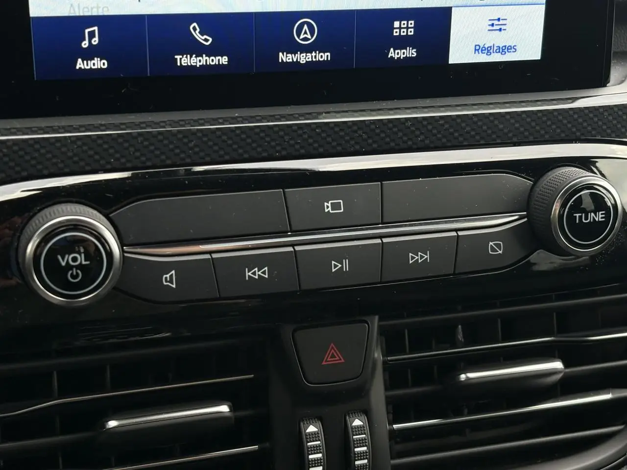 Vue rapprochée de la console centrale du Ford Kuga 2023, boutons audio noirs avec écran tactile visible en haut.