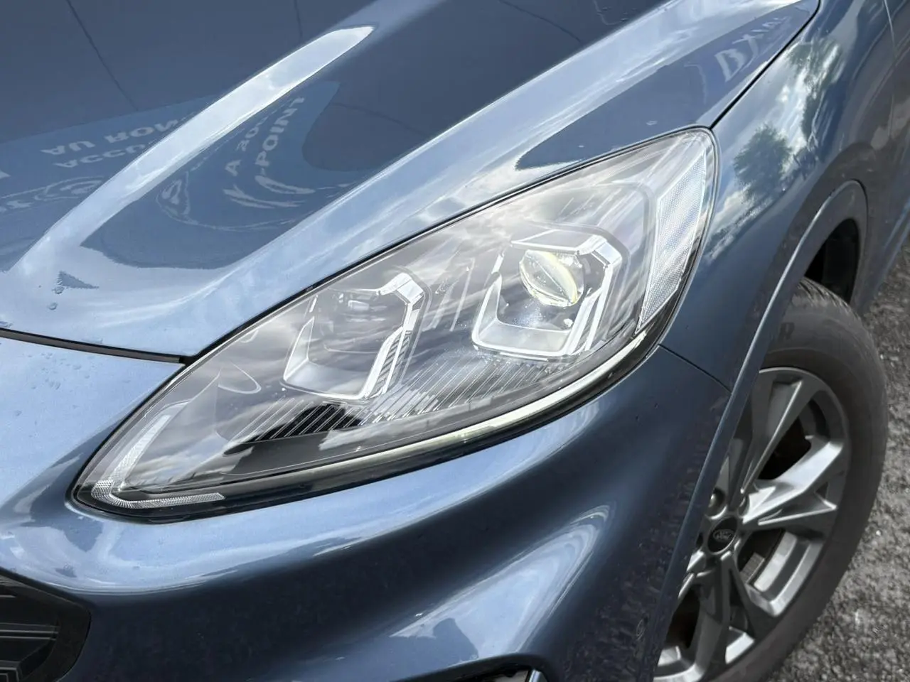 Gros plan sur le phare avant droit et la roue alliage 18 pouces d'un Ford Kuga 2.0 EcoBlue bleu azur 2023.