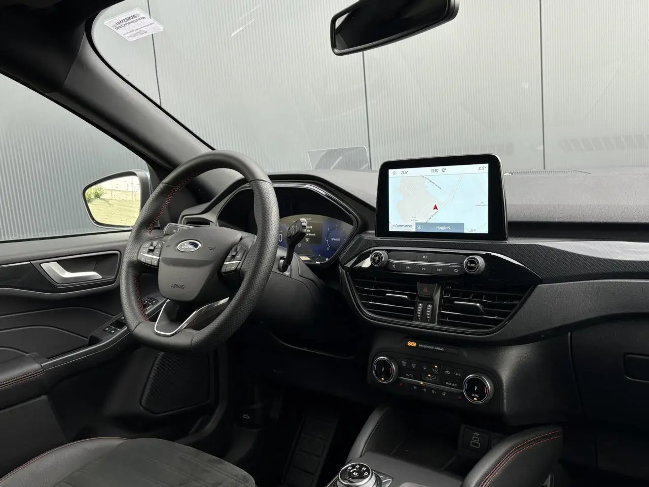 Vue intérieure côté conducteur du Ford Kuga 2023, volant ST-Line avec surpiqûres rouges et écran tactile GPS central.