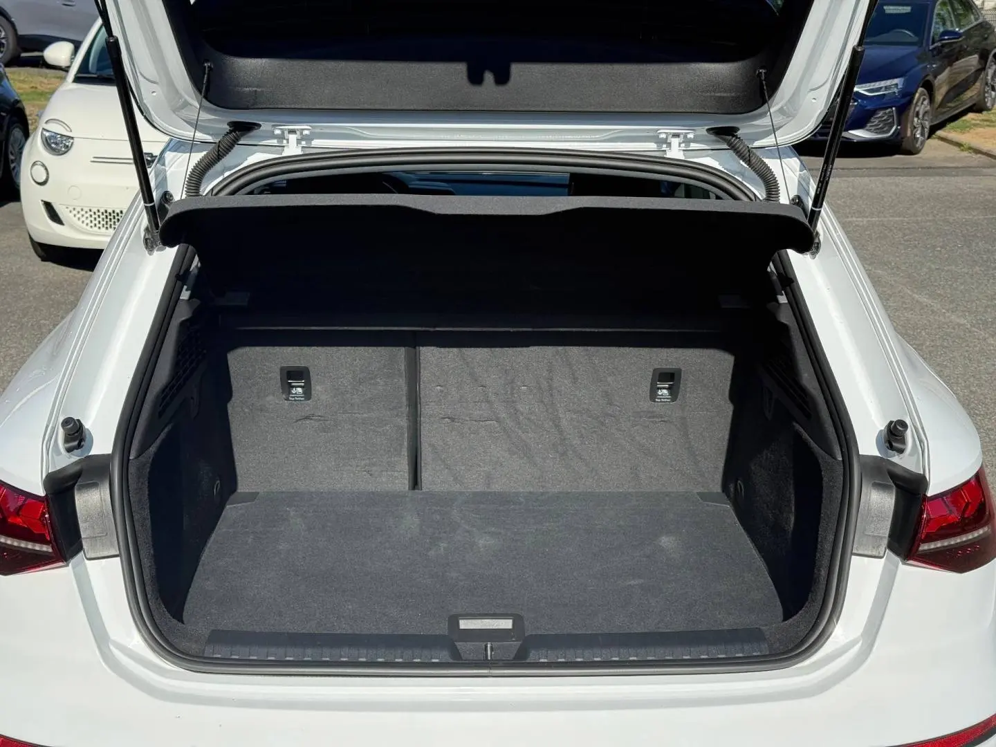 Coffre ouvert vu de l'arrière d'une Audi A3 Sportback blanche Arkona 2024, intérieur noir et spacieux.