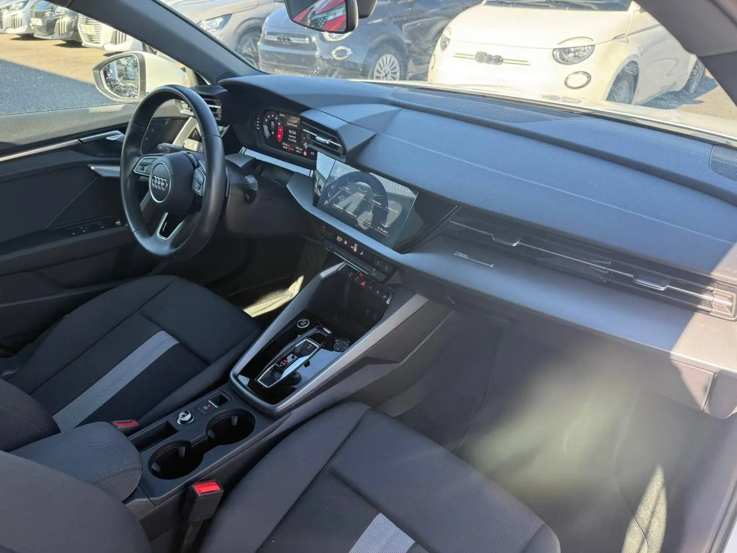 Vue intérieure côté conducteur de l'Audi A3 Sportback 2024, avec tableau de bord noir et écran tactile central.