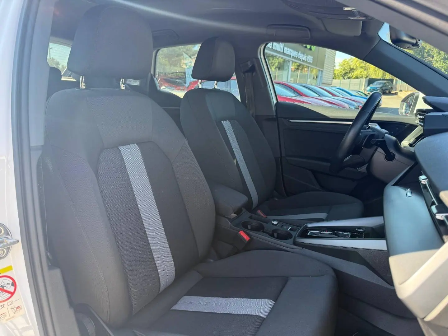 Vue intérieure côté conducteur de l'Audi A3 Sportback 2024, sièges tissu noir avec bande grise centrale et console moderne.